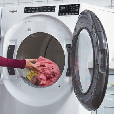 Hand putting items of clothing into a front load dryer