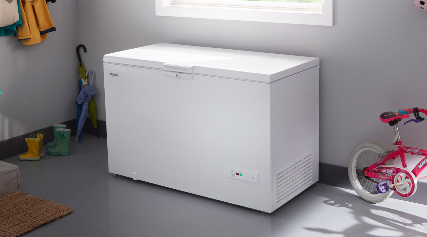 A deep freezer in a garage next to a bicycle and umbrellas