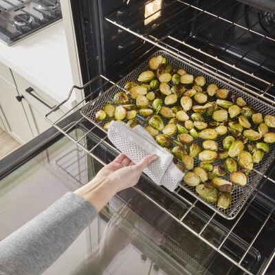 Person removing Brussels sprouts from an oven