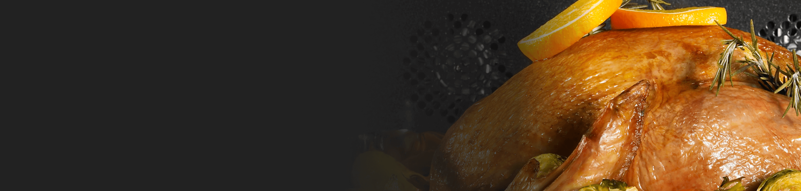 A turkey cooking in an oven garnished in rosemary and orange slices