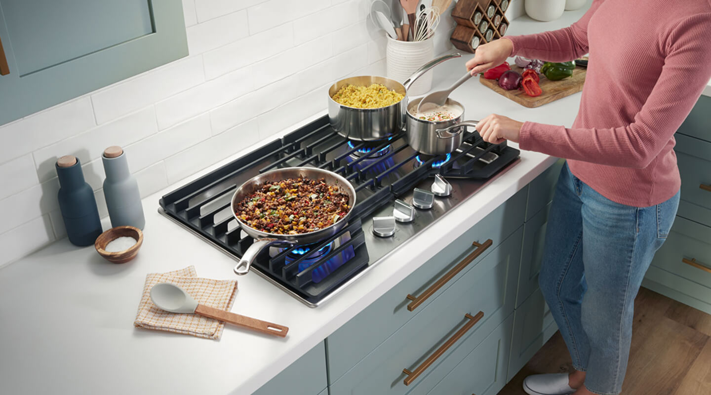 A person cooking food on their Whirlpool® Gas Cooktop