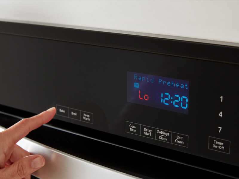 A finger pushing a button on the display of an oven