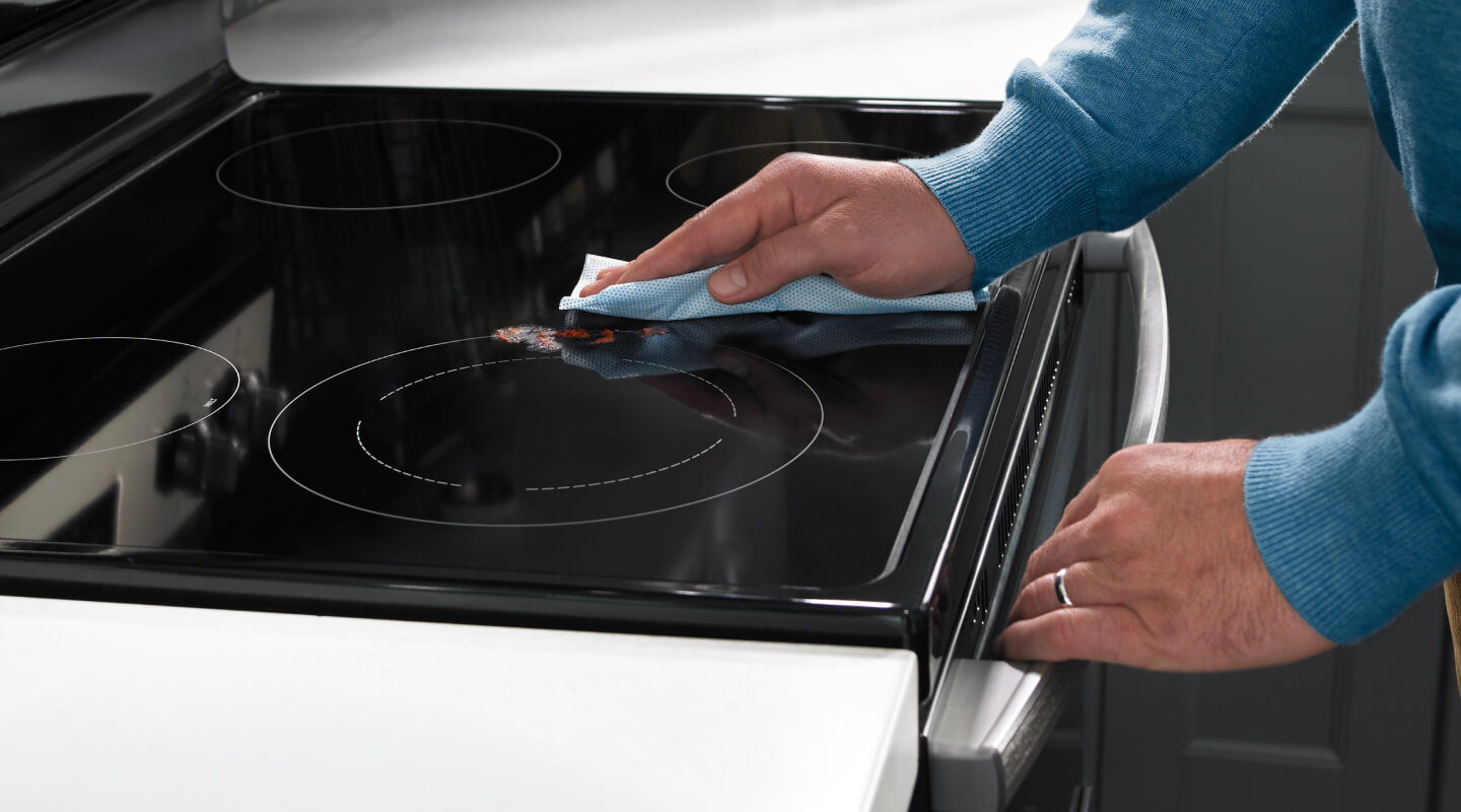 A hand wiping the cooking surface of an electric range