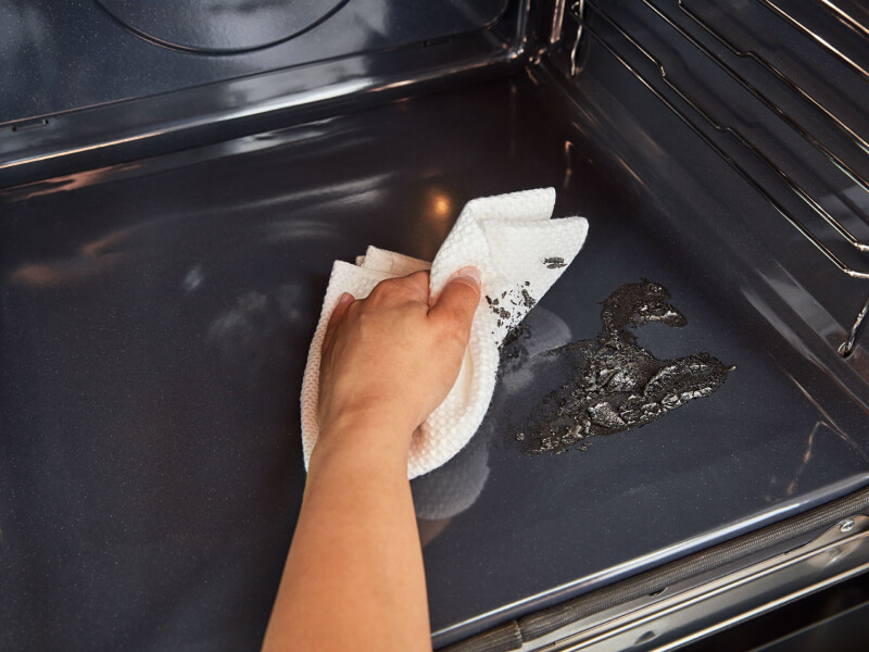 A hand wiping the inside of an oven A hand wiping the inside of an oven