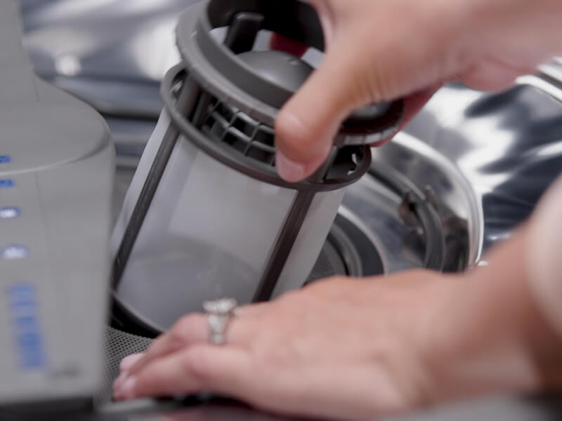 A person removing a filter from a dishwasher