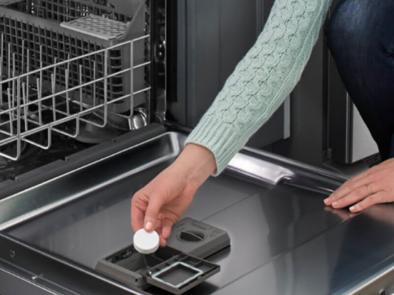 A person adding a dishwasher cleaner tablet to a dishwasher
