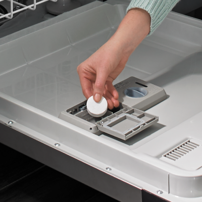 A person adding a dishwasher cleaner tablet to a dishwasher