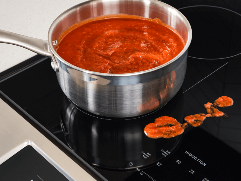 Sauce in a pan on an induction stovetop, next to splatter on the stovetop Sauce in a pan on an induction stovetop, next to splatter on the stovetop