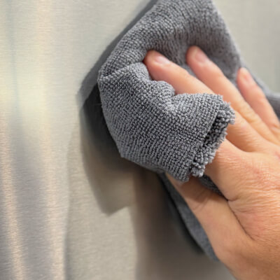 Close up of a hand using a towel to clean a stainless steel appliance