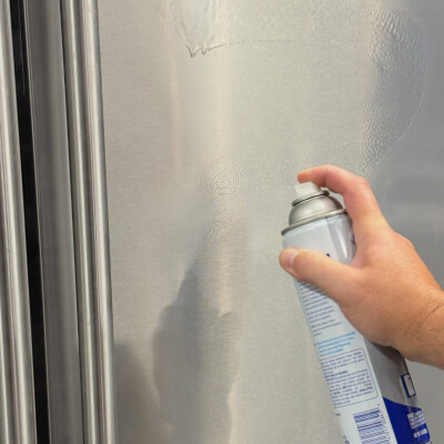 Hand spraying affresh® stainless steel cleaner onto refrigerator