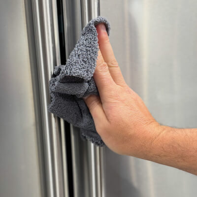 Hand wiping a stainless steel refrigerator with a dry cloth