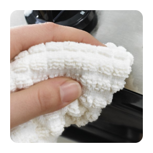 Close up of a hand using a towel to clean a stainless steel appliance 