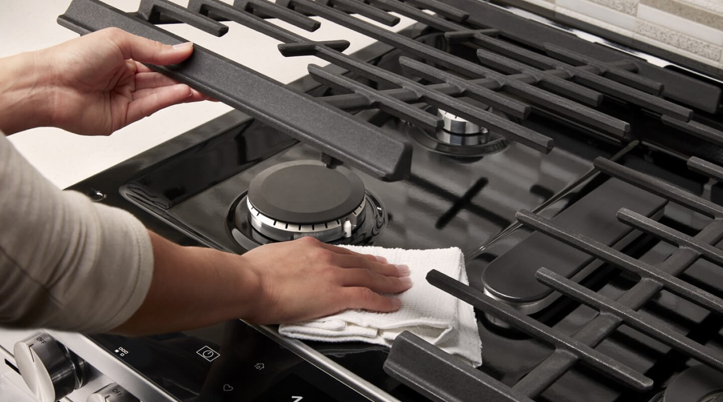 Person lifting grates to clean gas stovetop