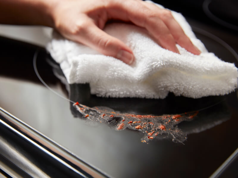 Person cleaning a mess on an electric cooktop Person cleaning a mess on an electric cooktop