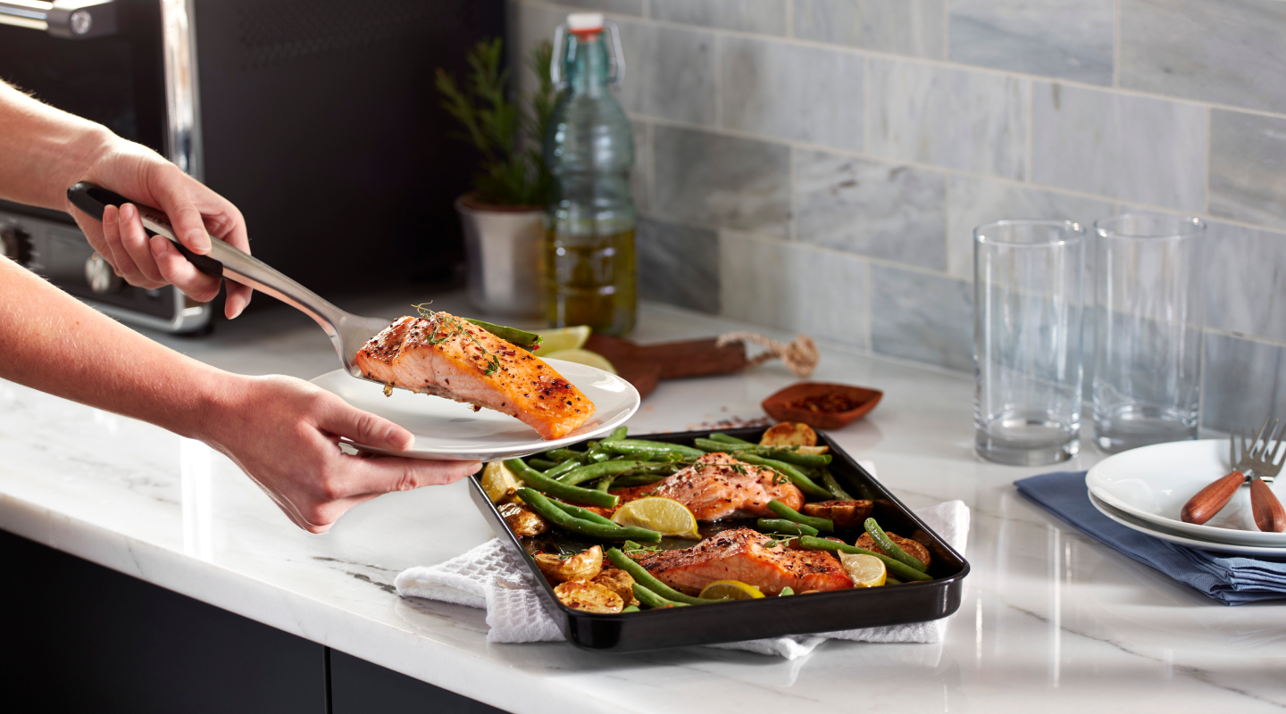 Person placing a piece of cooked salmon on a plate Person placing a piece of cooked salmon on a plate