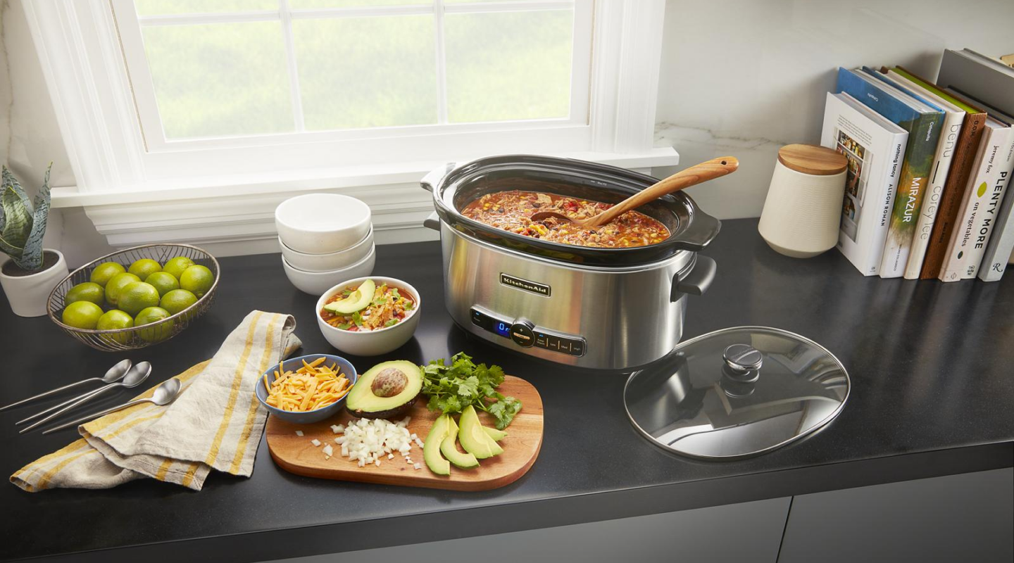 Slow cooker filled with chili next to a cutting board with toppings Slow cooker filled with chili next to a cutting board with toppings