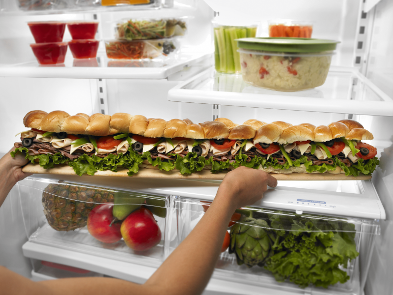 Person placing a party sub sandwich in a refrigerator Person placing a party sub sandwich in a refrigerator