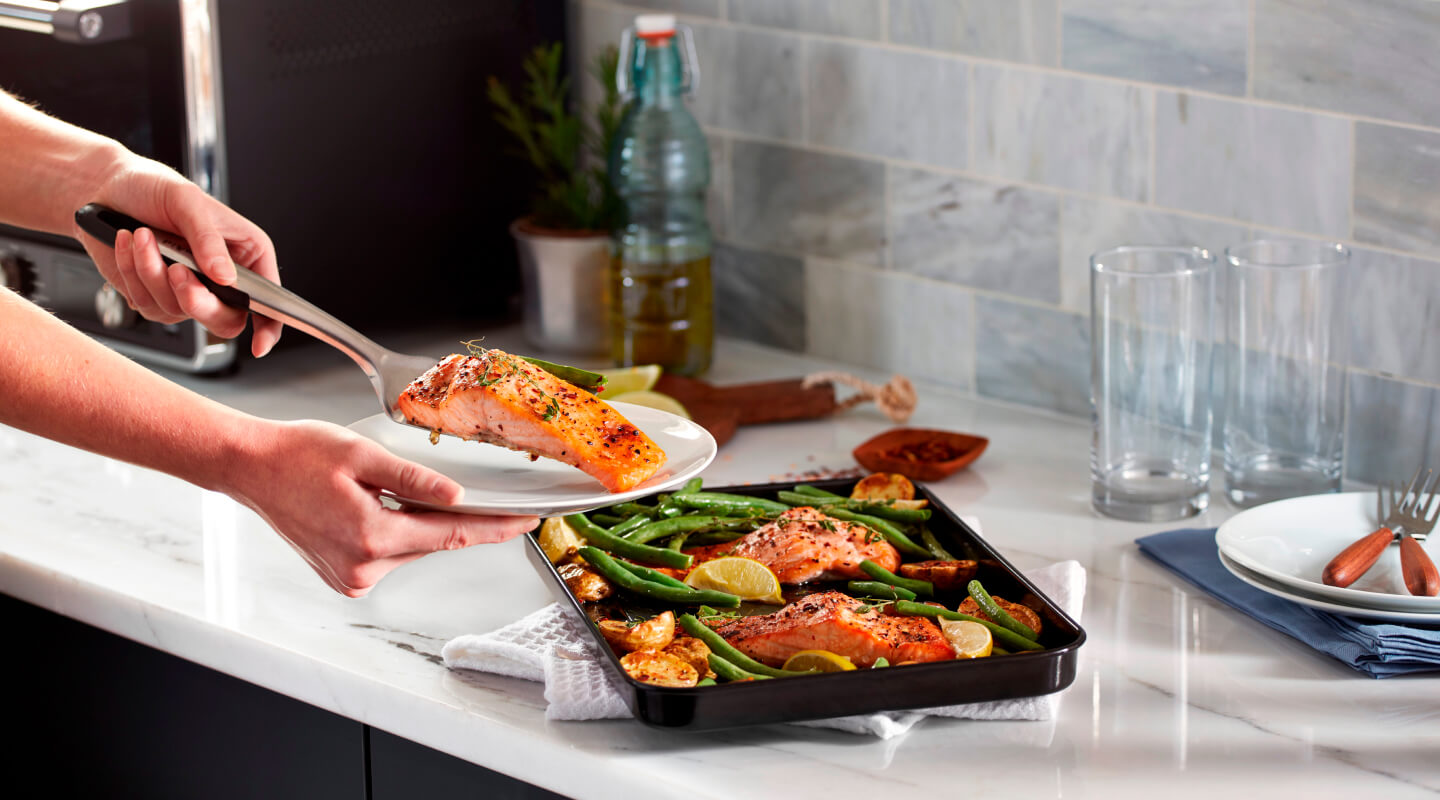 Person placing a piece of cooked salmon on a plate