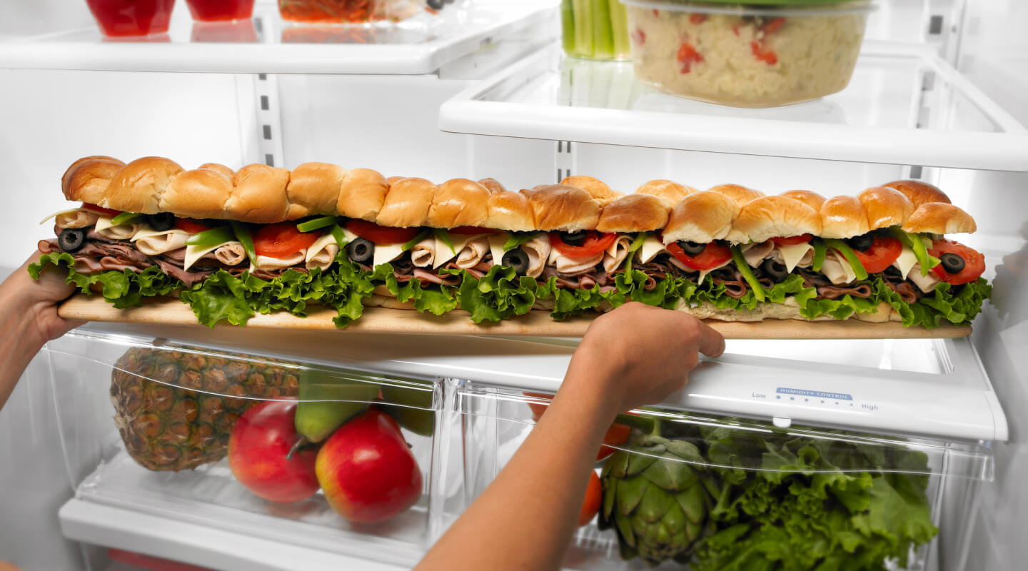Person placing a party sub sandwich in a refrigerator