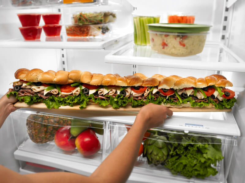 Person placing a party sub sandwich in a refrigerator