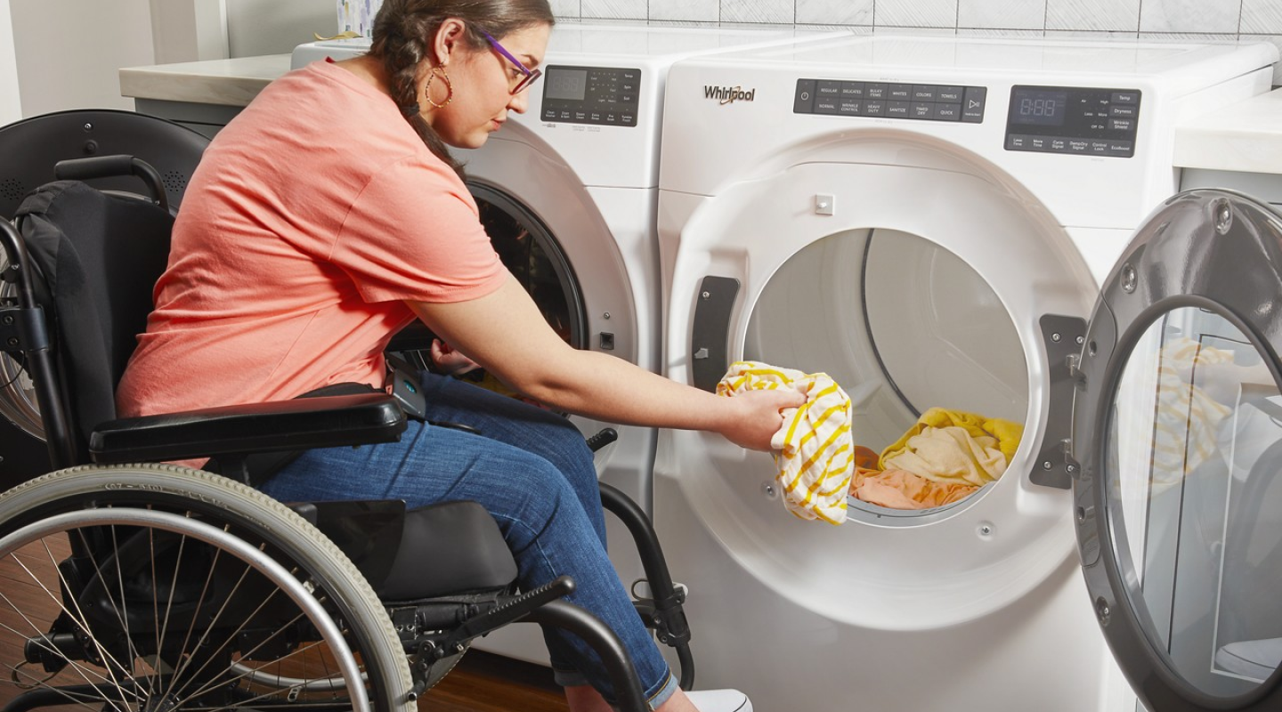 Woman in a wheelchair loading her Whirlpool® dryer with clothing.
