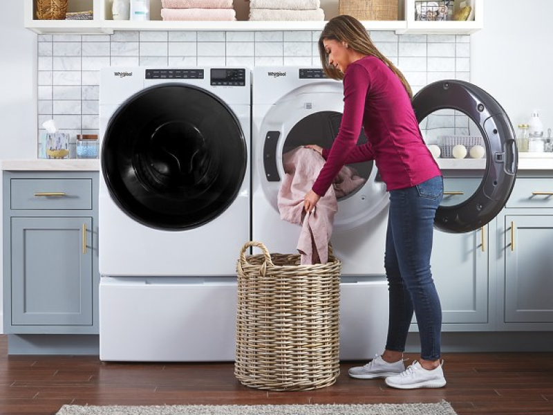 Woman loading sheets into laundry basket from dryer.