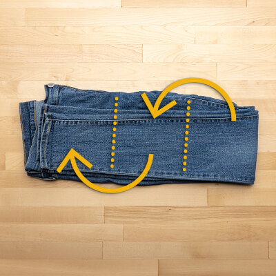 A pair of jeans folded in half, with arrows directing to fold in thirds