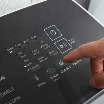 A finger hovering over cycle settings on a washer panel