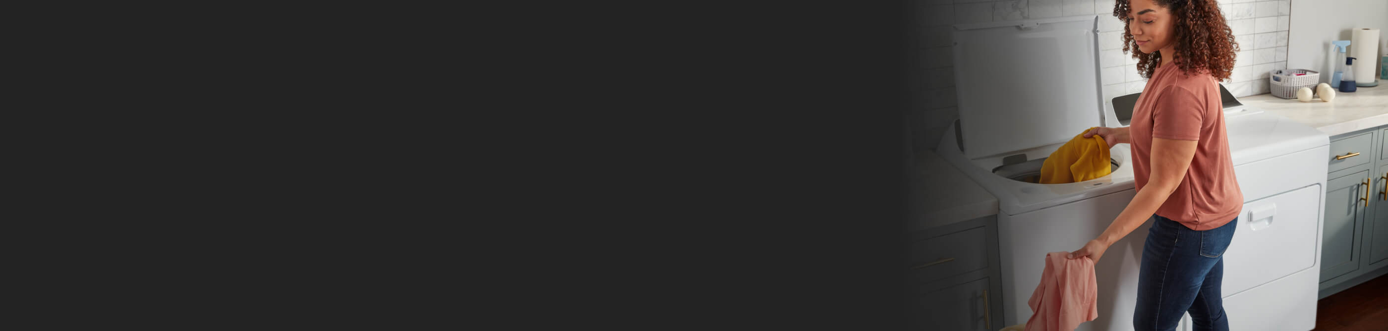 A person loading orange and pink linens into a white top load washer next to a white front load dryer