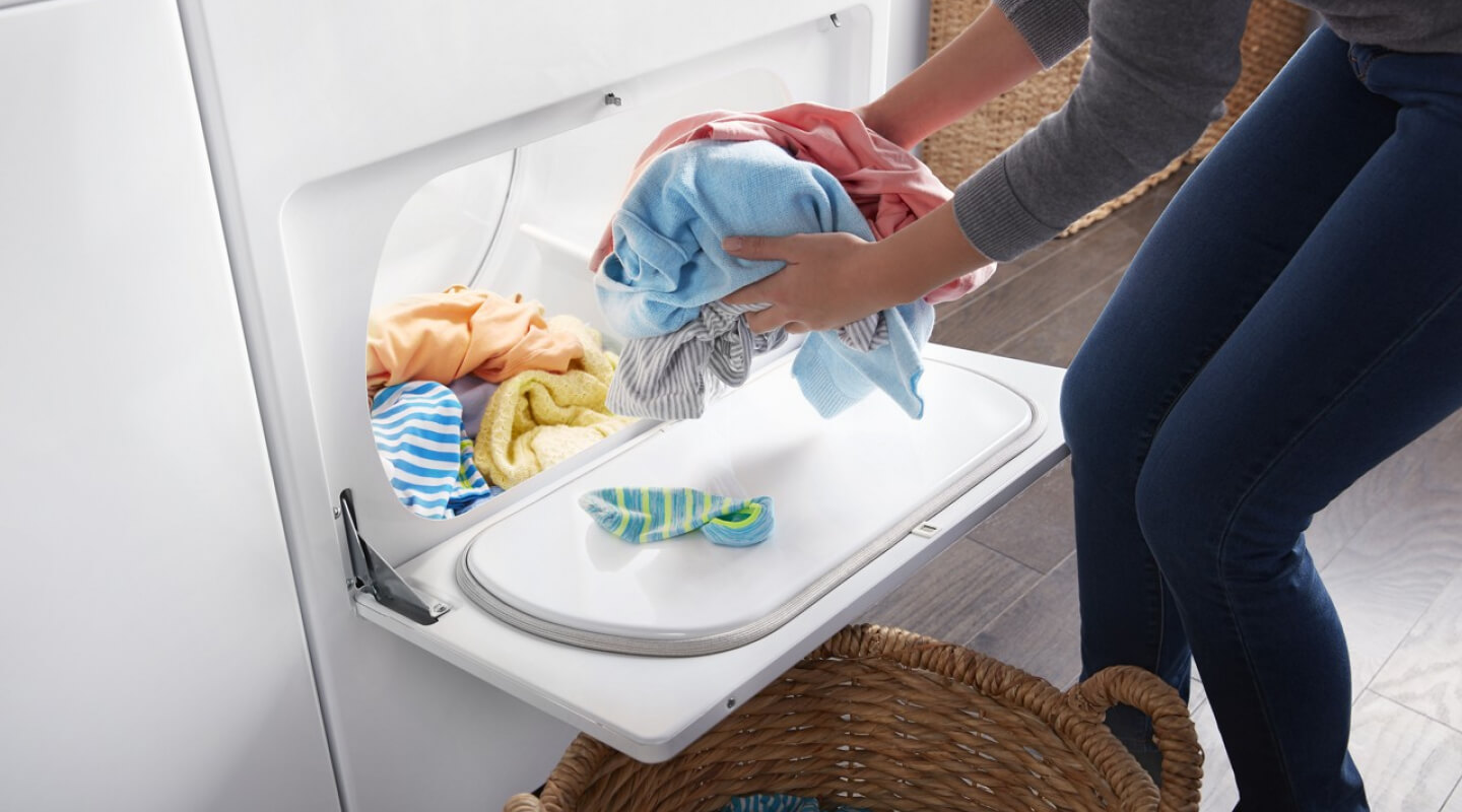 Person removing dry clothes from a dryer and placing them in a basket Person removing dry clothes from a dryer and placing them in a basket