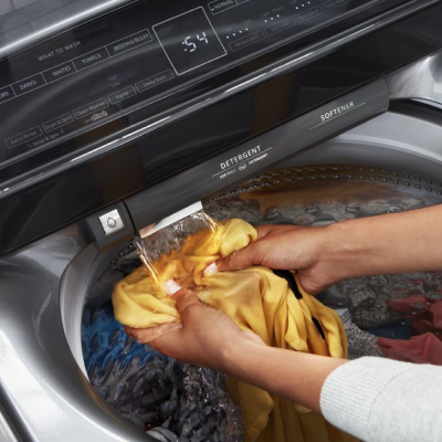 Person rinsing a garment under a built-in water faucet in a Whirlpool® Washer