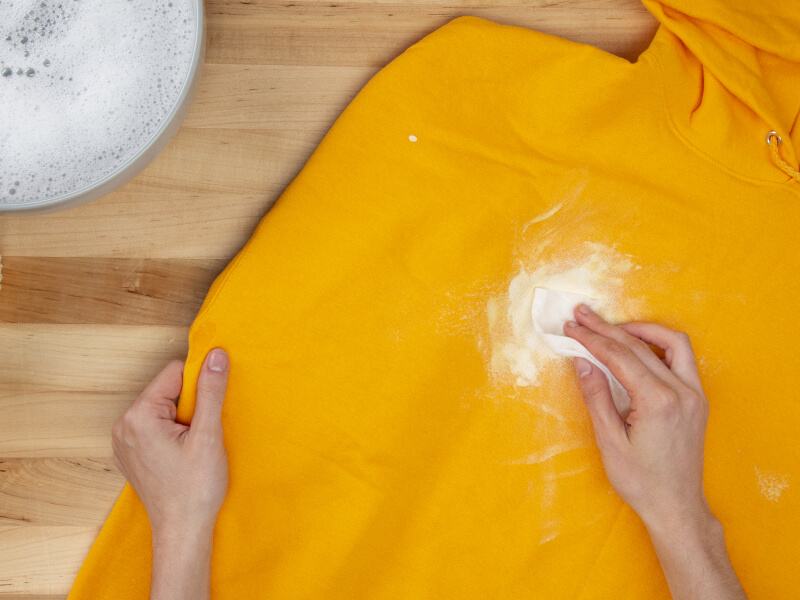 Hand blotting white paint on a yellow sweatshirt with a paper towel Hand blotting white paint on a yellow sweatshirt with a paper towel