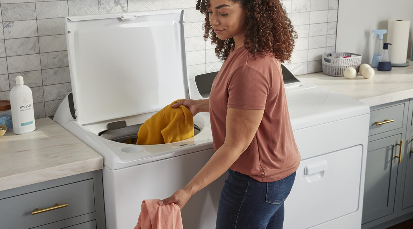 A person doing laundry with a top load washer and dryer