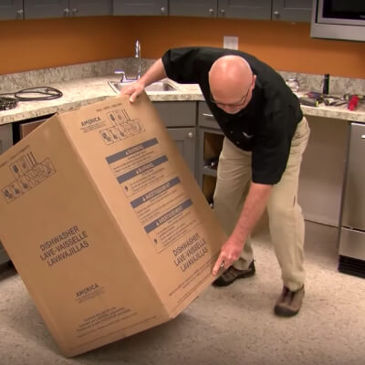 A person tilting a dishwasher cardboard box on its side