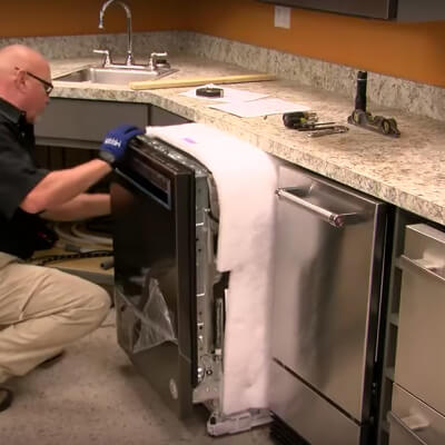 A person sliding a dishwasher into a cutout space