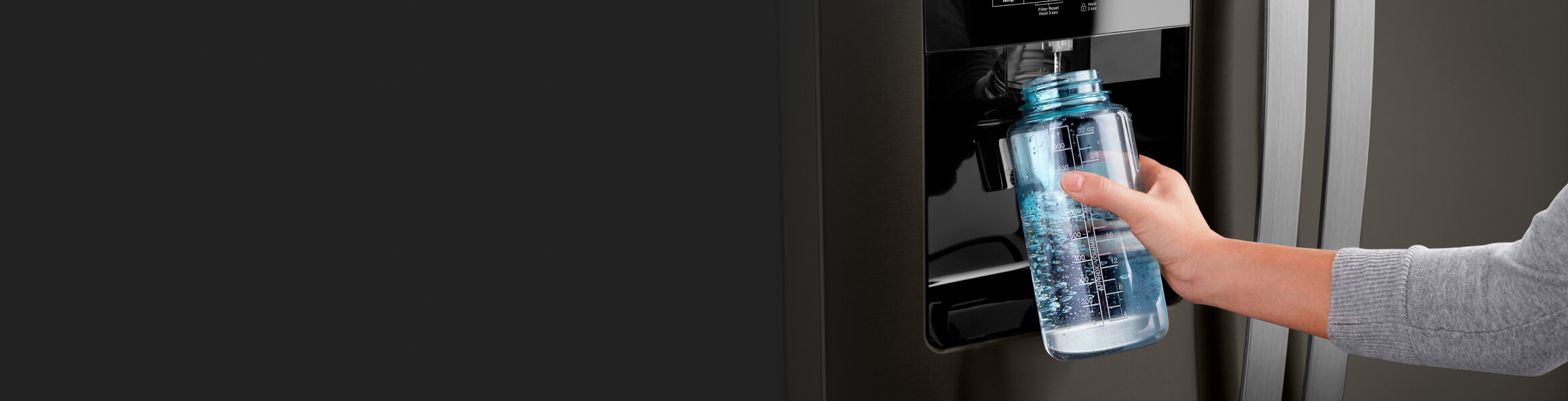 A person filling up their water bottle from the fridge