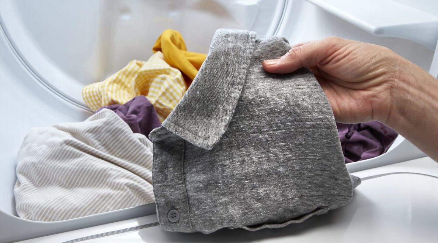 Person taking a gray shirt out of a dryer Person taking a gray shirt out of a dryer