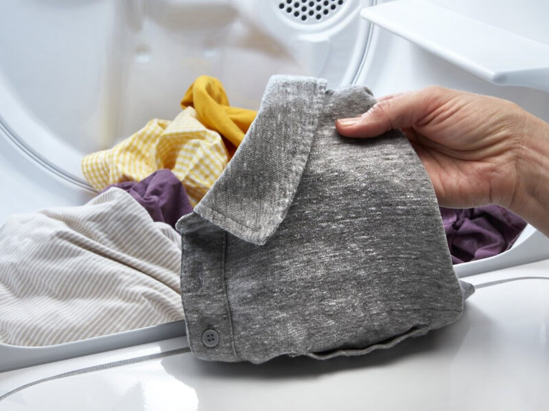 Person taking a gray shirt out of a dryer Person taking a gray shirt out of a dryer
