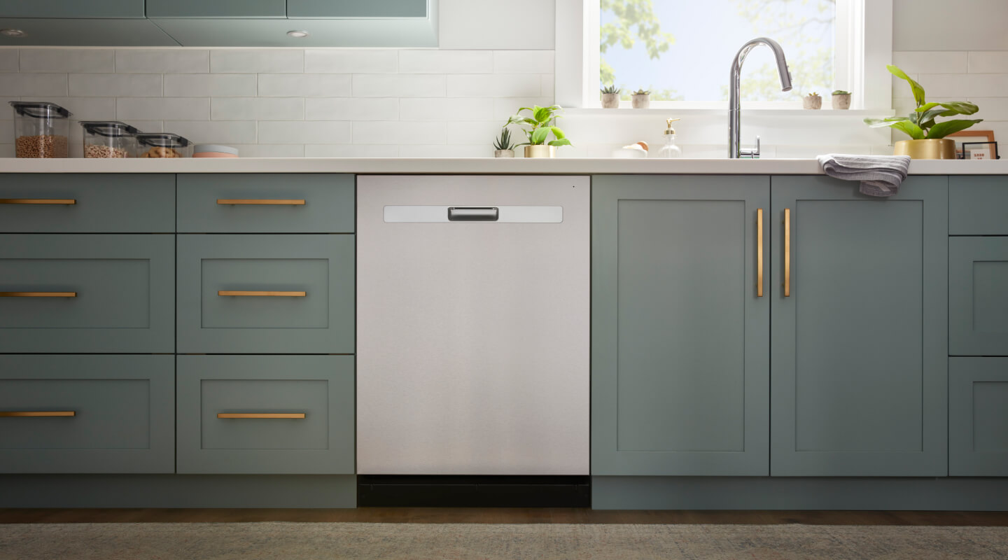 The inside of a kitchen with sage green cabinetry and a stainless steel dishwasher