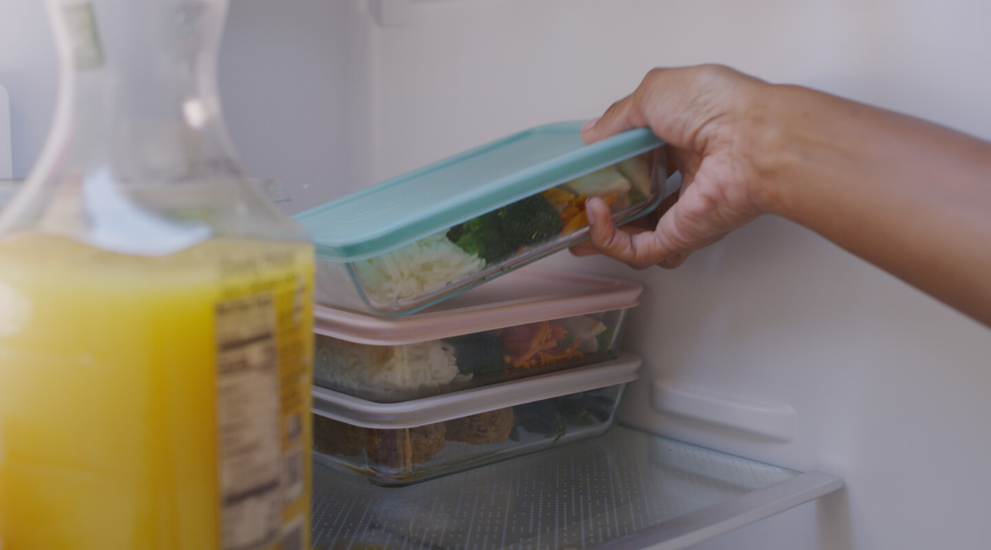 Hand storing meal prep container into fridge