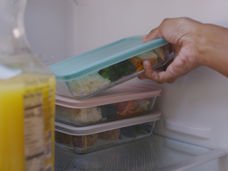 Hand storing meal prep container into fridge