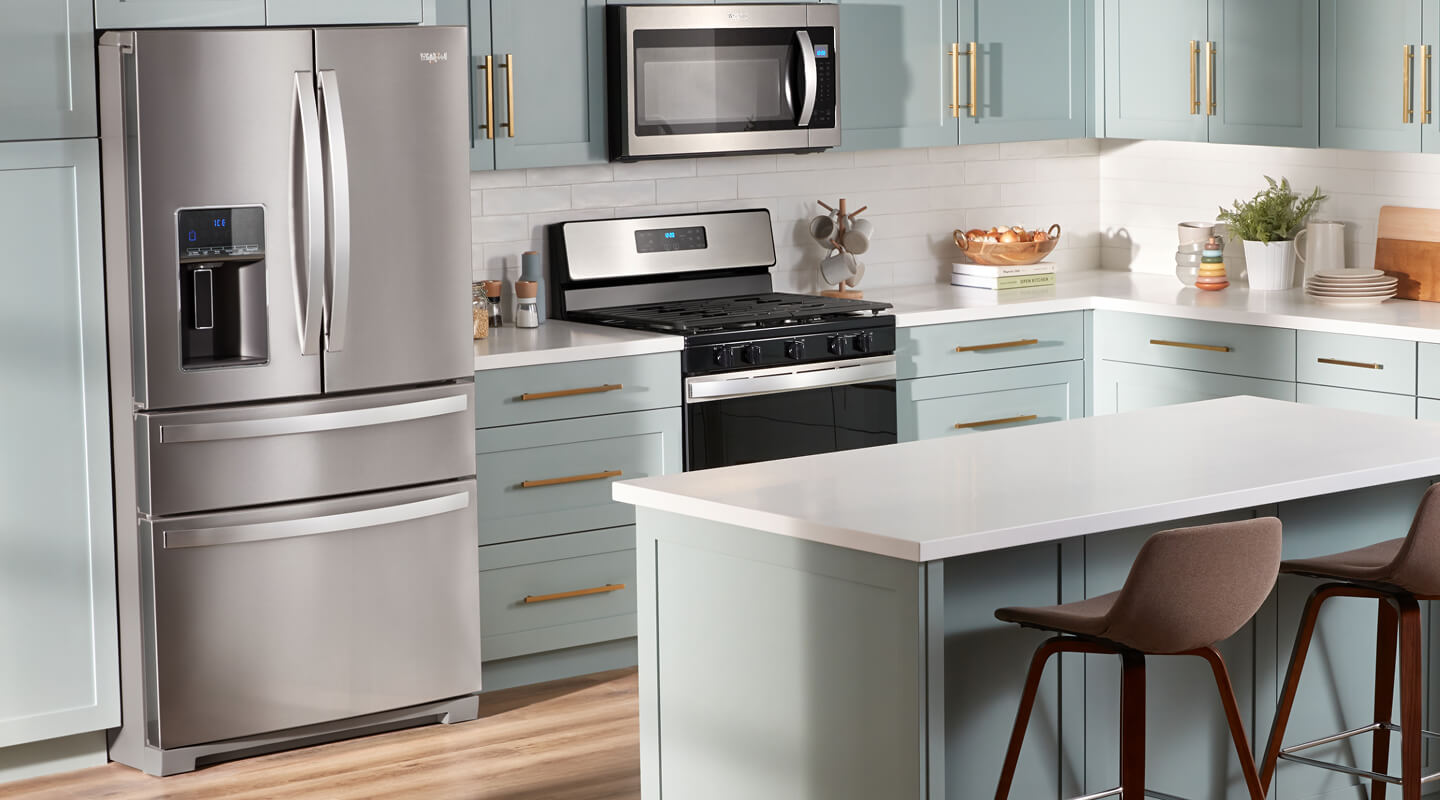 A stainless steel 4 door refrigerator in a bright kitchen with light blue cabinetry