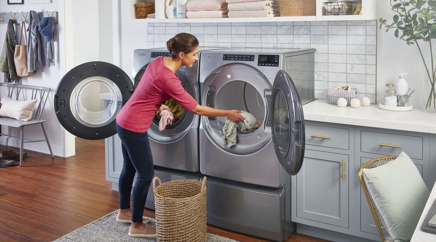 A woman moving clothes from her washer to her dryer