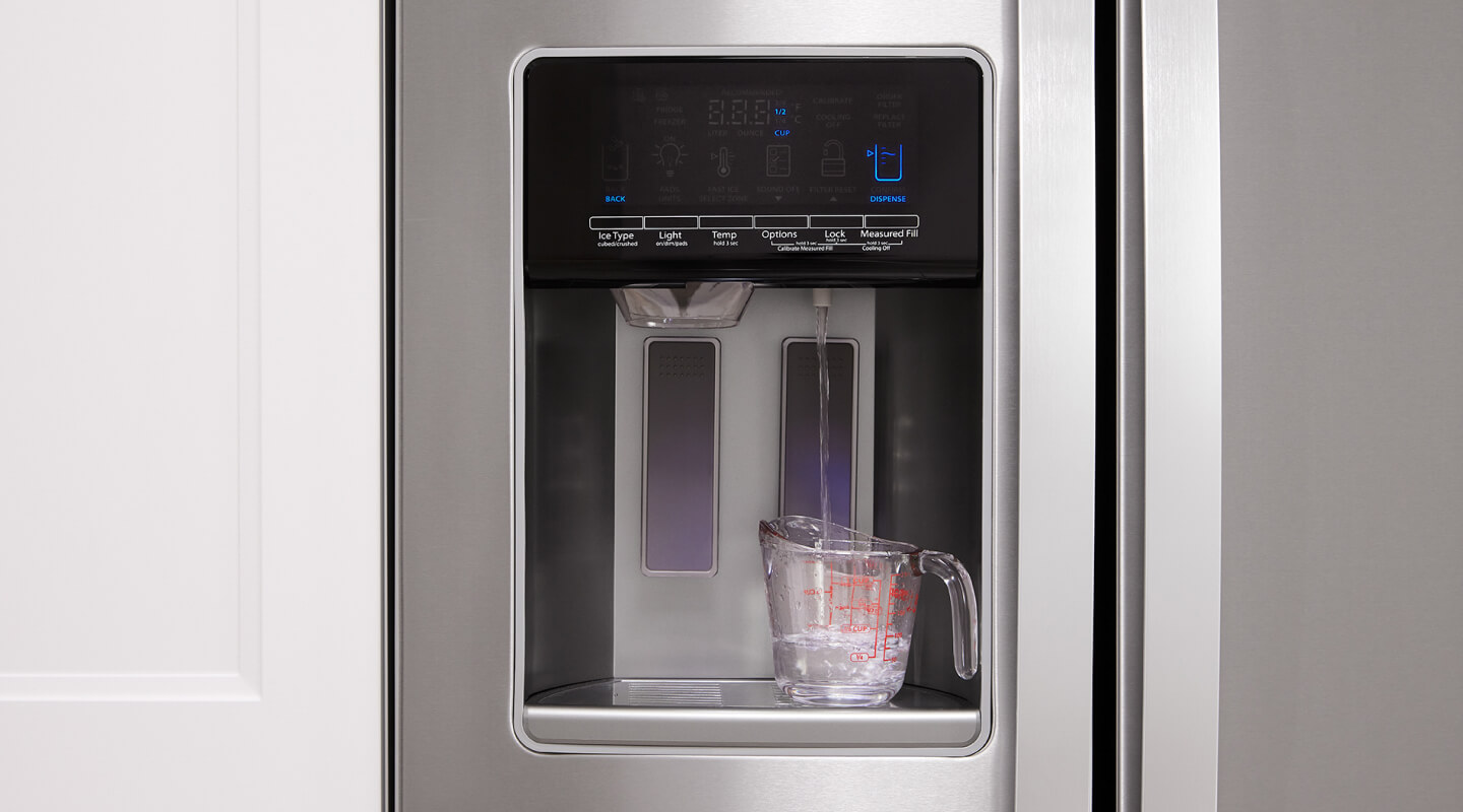 A measuring cup being filled with water from a side-by-side refrigerator's exterior dispenser