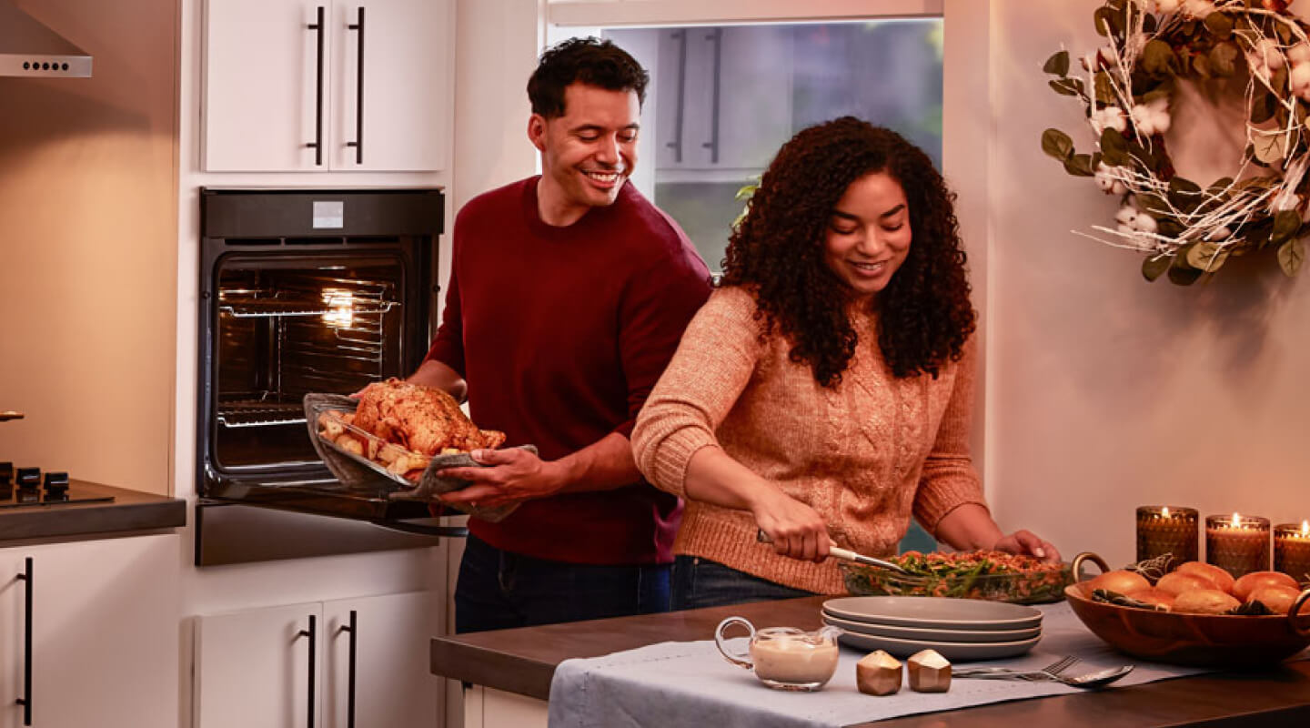 A couple preparing a dinner of roasted chicken, vegetables and bread rolls A couple preparing a dinner of roasted chicken, vegetables and bread rolls