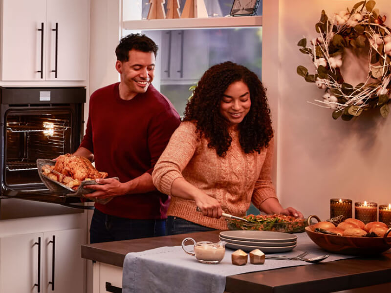 A couple preparing a dinner of roasted chicken, vegetables and bread rolls A couple preparing a dinner of roasted chicken, vegetables and bread rolls