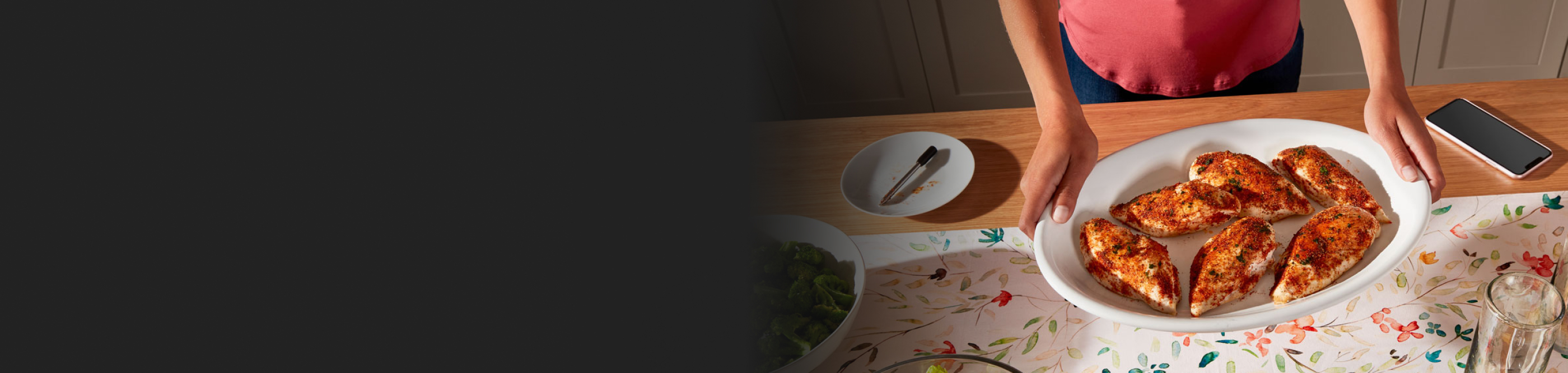 A person holding a tray of seasoned chicken breasts