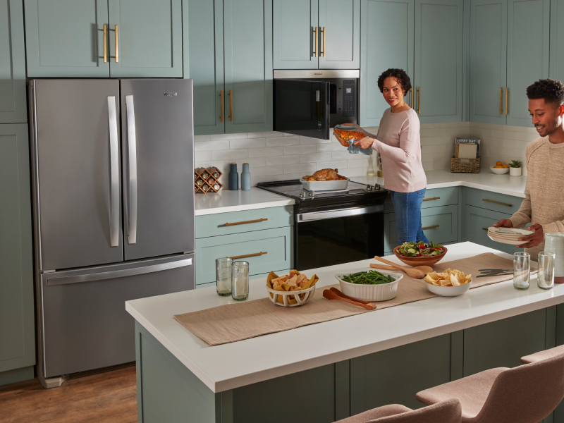 Two people cooking and preparing a meal in a kitchen with blue cabinets and white backsplash. Two people cooking and preparing a meal in a kitchen with blue cabinets and white backsplash.