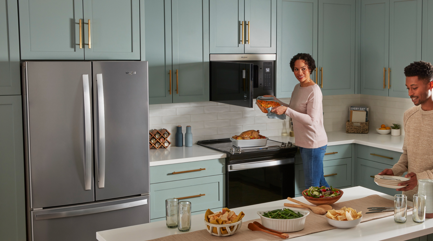 Two people cooking and preparing a meal in a kitchen with blue cabinets and white backsplash. Two people cooking and preparing a meal in a kitchen with blue cabinets and white backsplash.