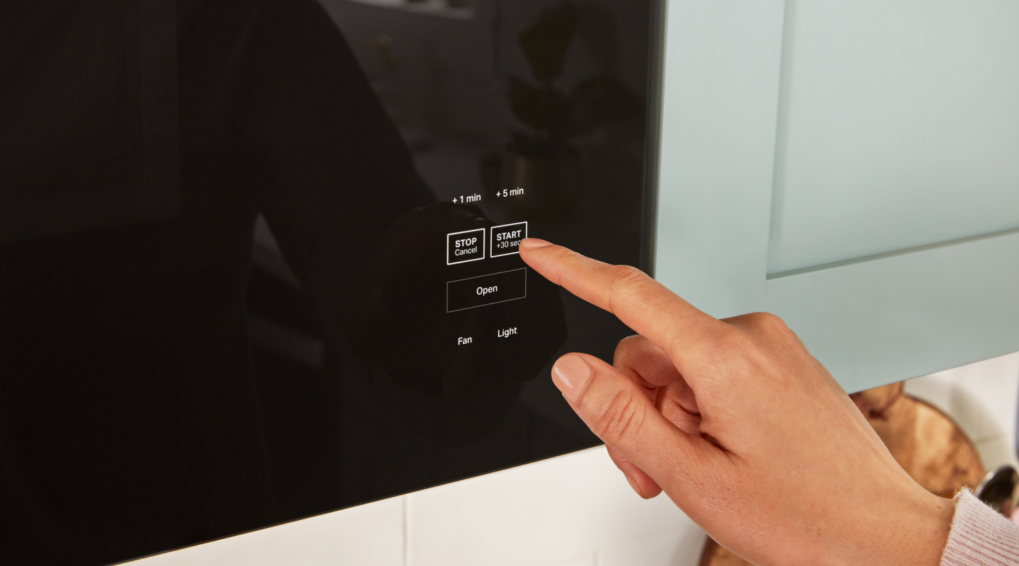 Person pressing start button on microwave